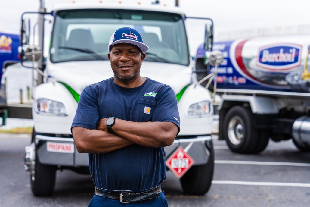Burch worker smiling with arms crossed in front of trucks